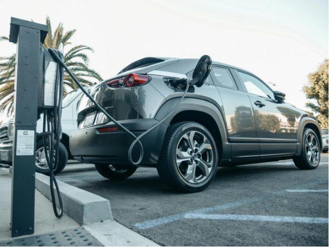 Electric car plugged into a public charging station on a sunny day, demonstrating eco-friendly transportation and modern EV technology.