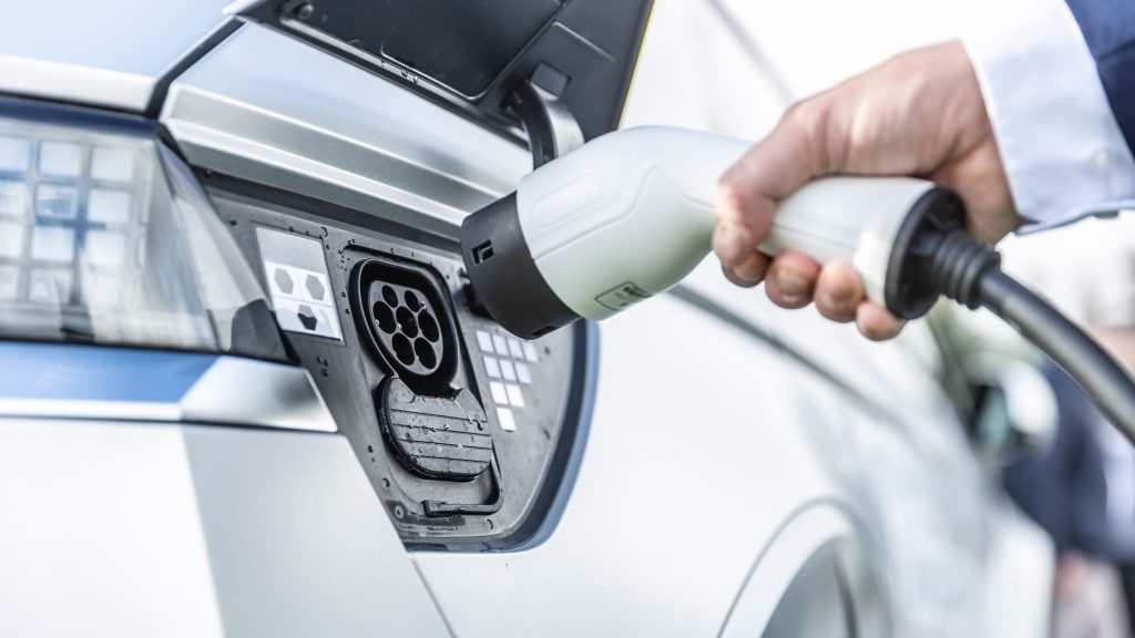 A man is holding the interface of a charging station, preparing to charge the car.