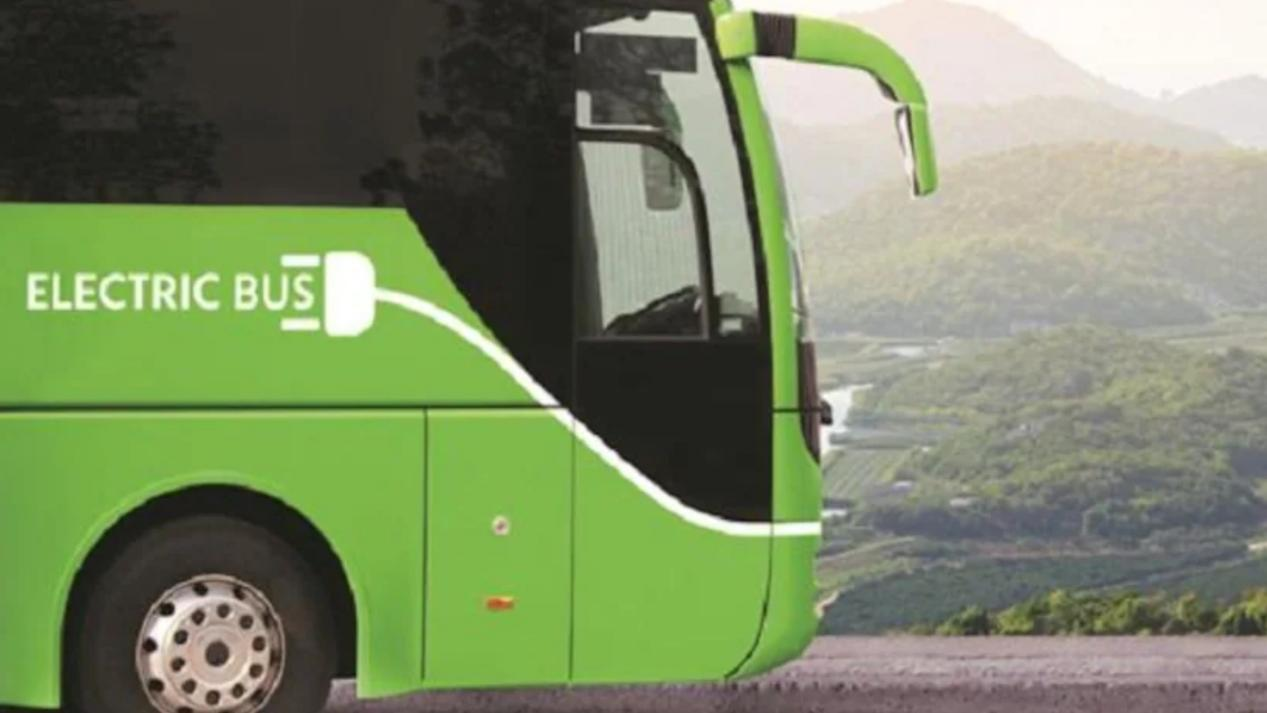 A green electric bus with a charging icon is parked against a scenic mountain background, highlighting eco-friendly transportation solutions. 