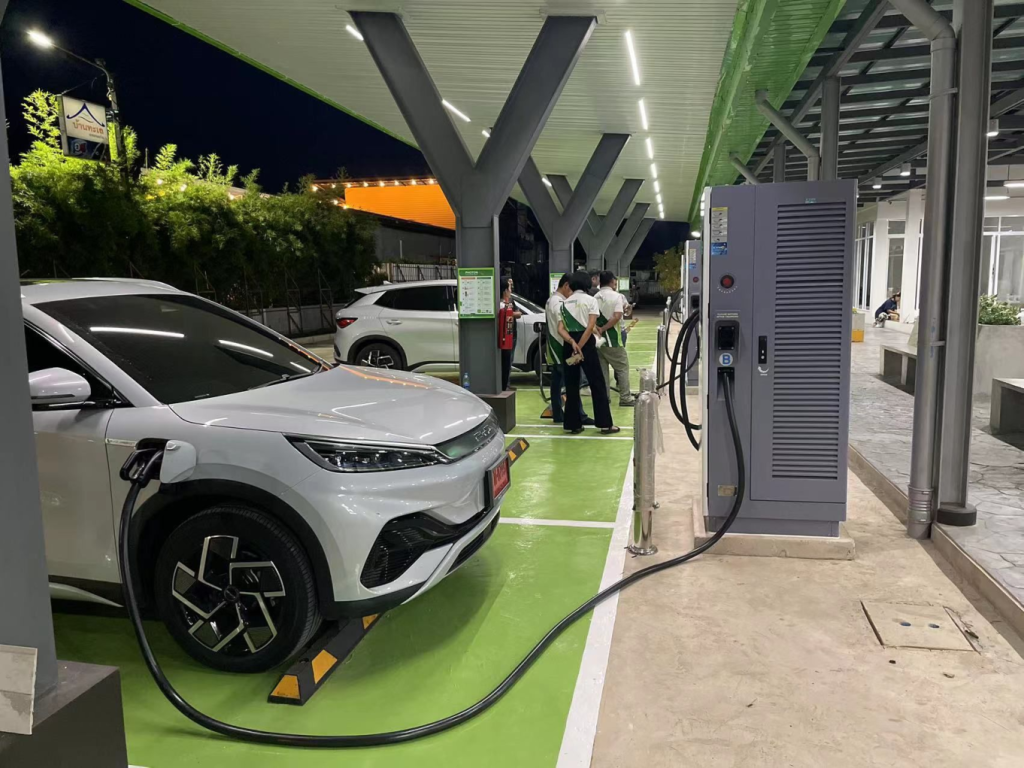 Electric vehicles charging at a DC fast charging station at night with technicians nearby.